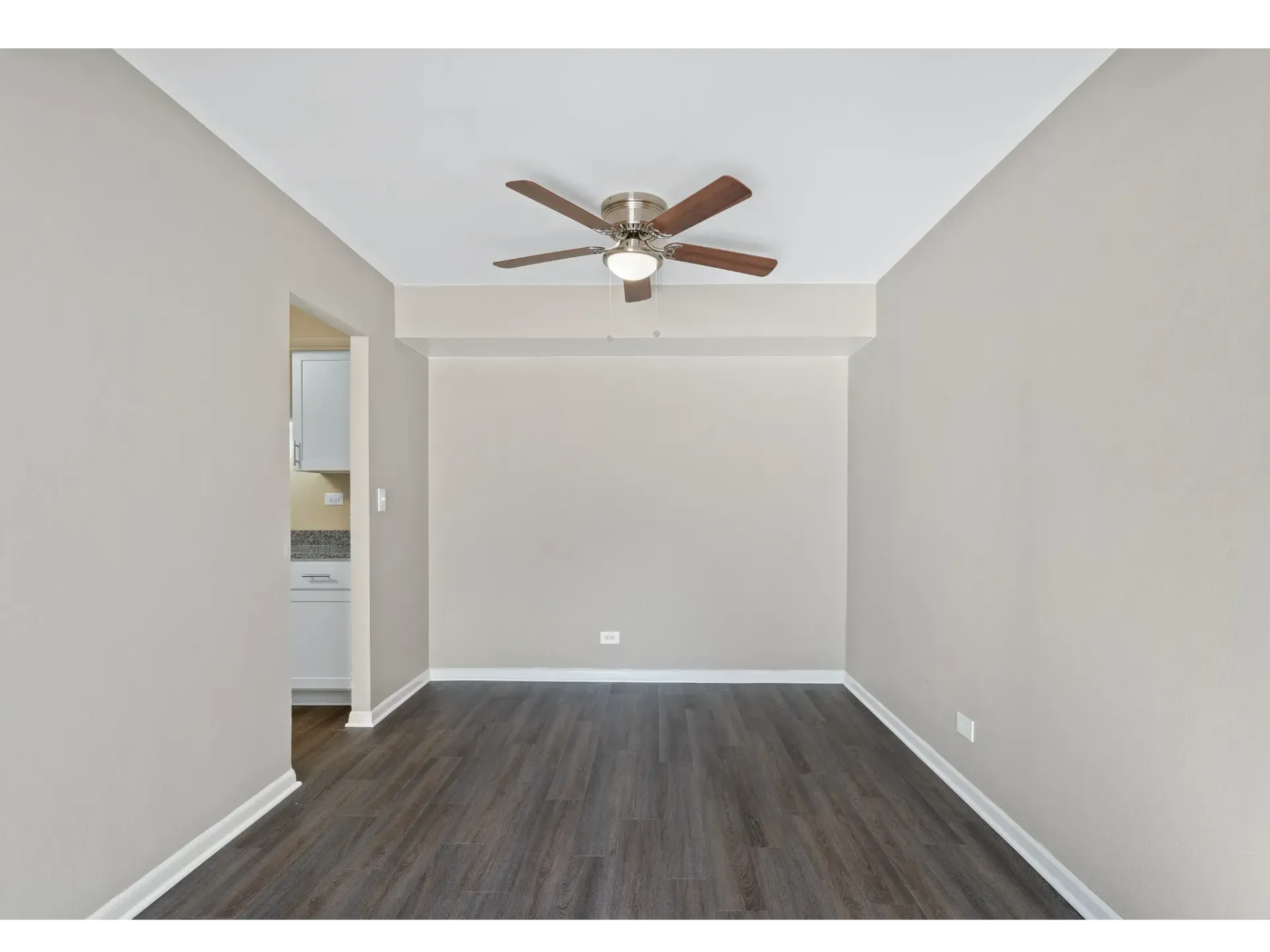 Interior view of an empty apartment living area with a ceiling fan and wood flooring.