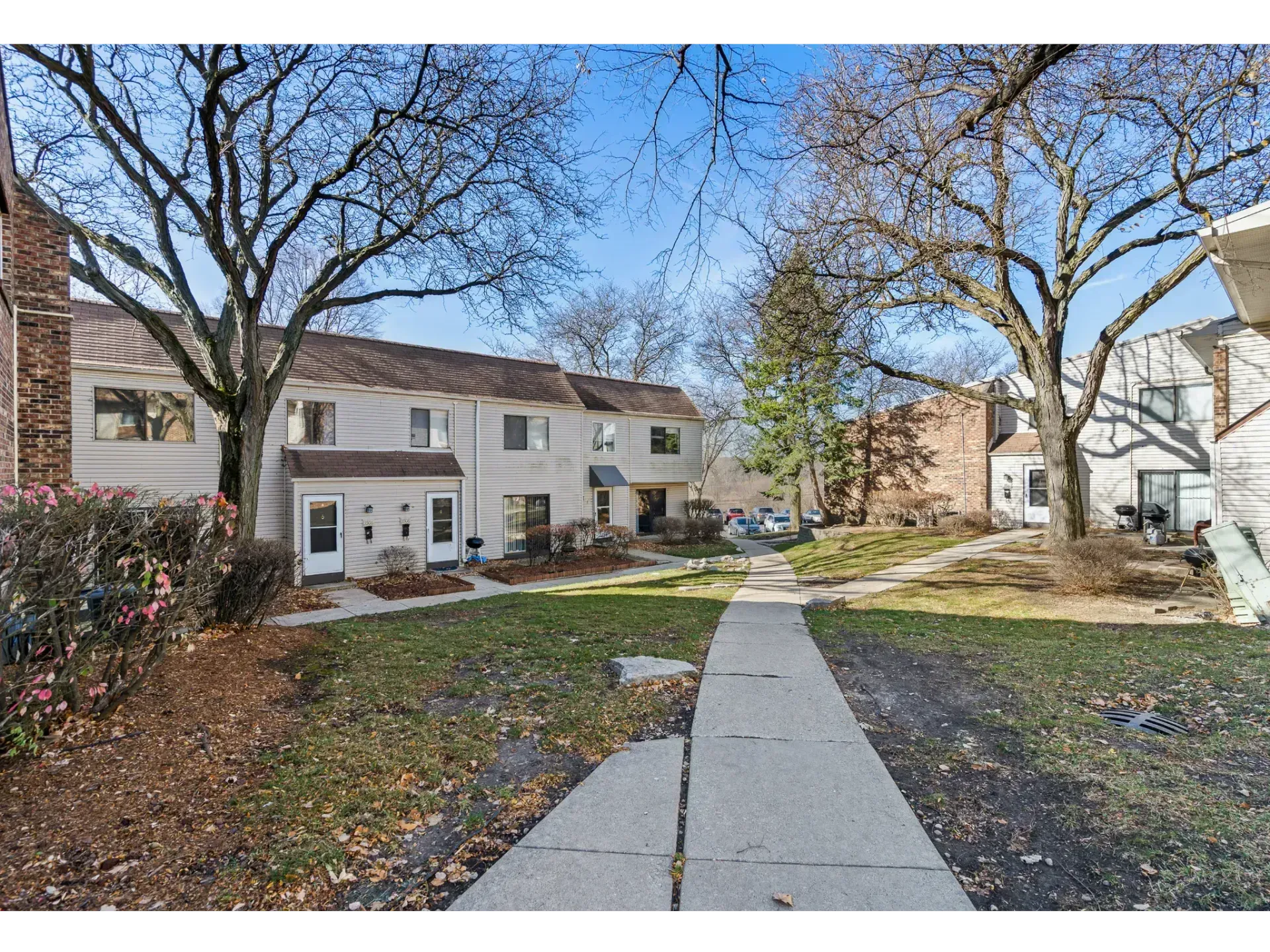 Apartment courtyard with brick and white buildings, leafless trees, and a concrete walkway under a clear blue sky