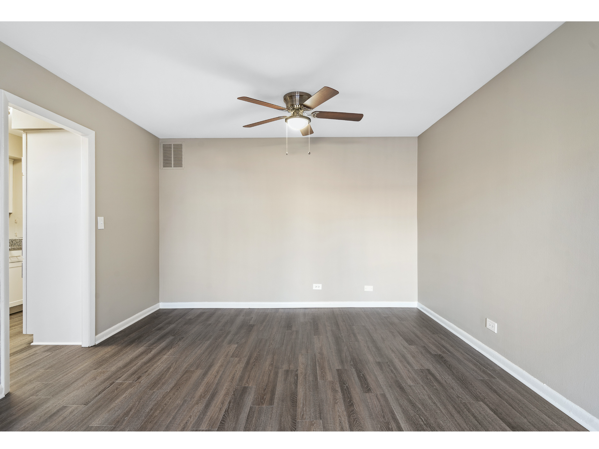 Empty beige living room with wood-look flooring, ceiling fan, and doorway to a hall.