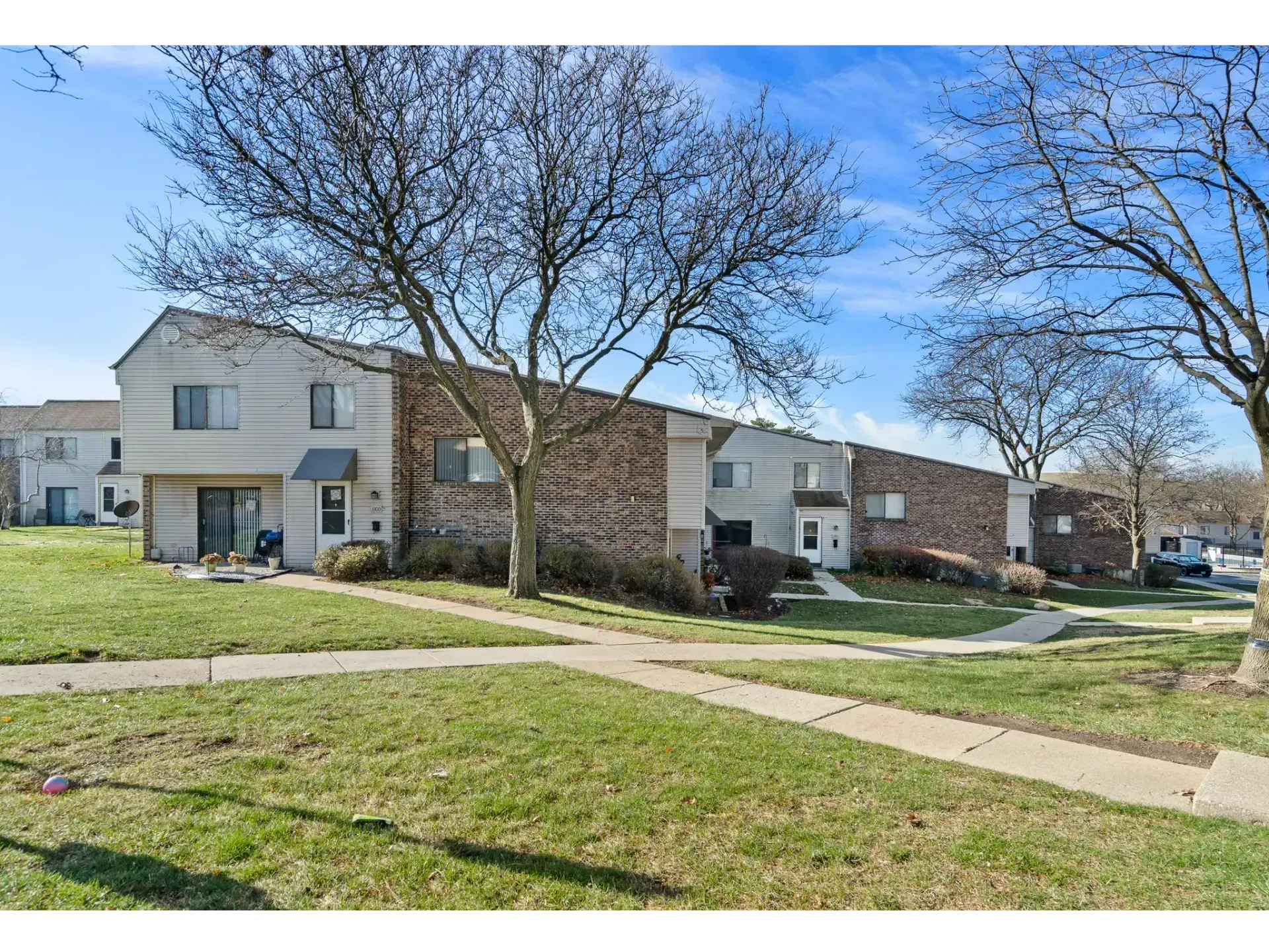 Row of two-story apartment buildings with leafless trees and grassy courtyard under a blue sky
