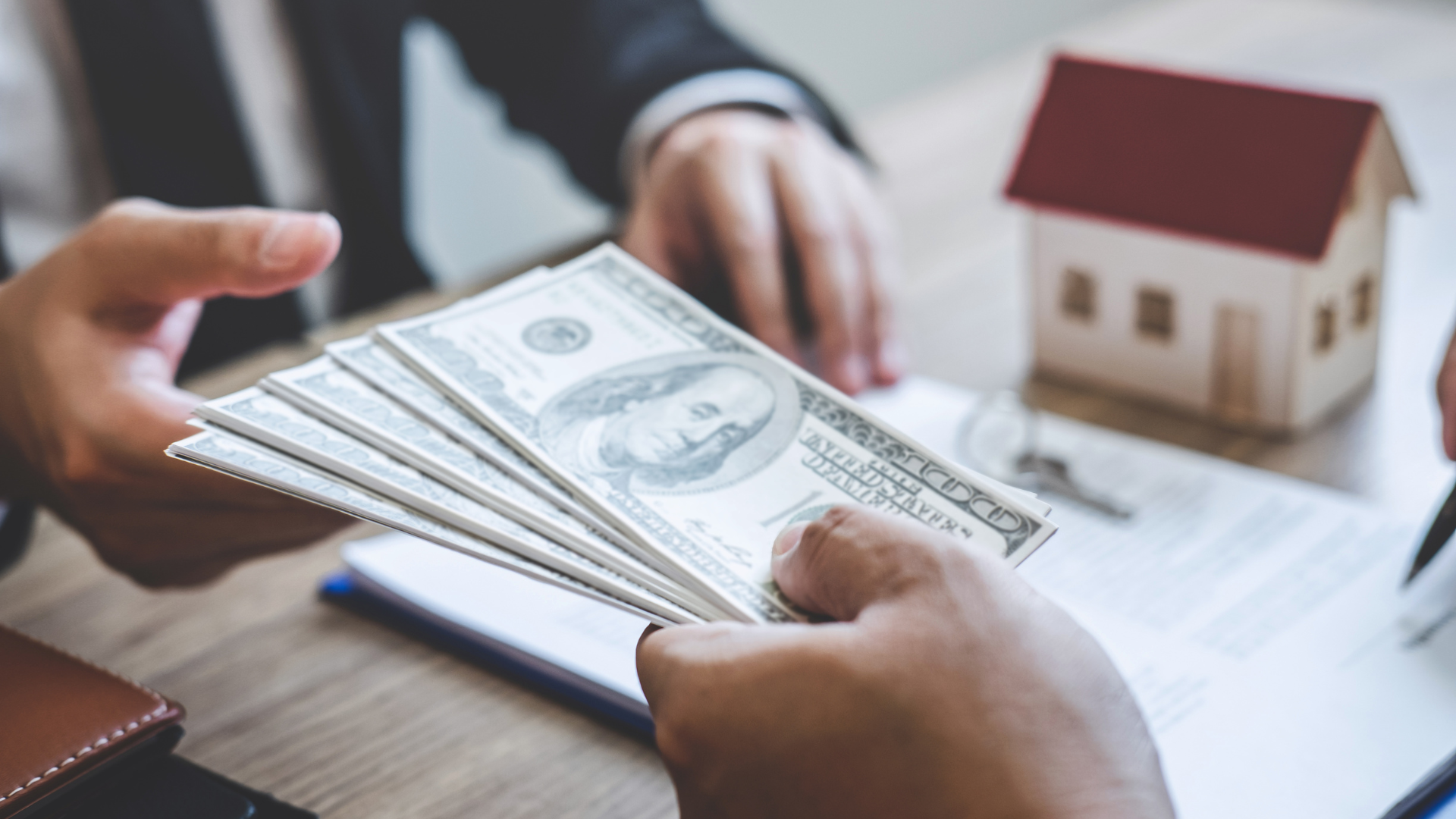 Two-story beige house with red tile roof and palm trees under a blue sky with clouds.