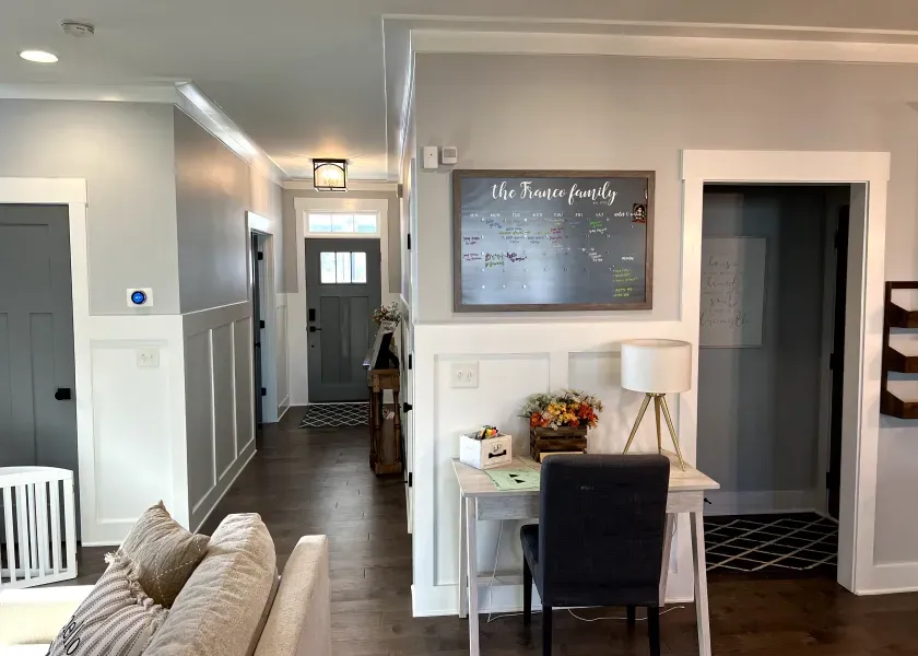 Hallway with gray walls, white trim, and a desk with a framed family calendar and flowers.