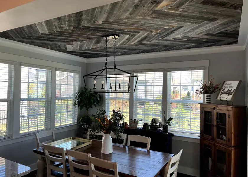 Dining room with wood-paneled ceiling, large windows, wooden table, and a chandelier.