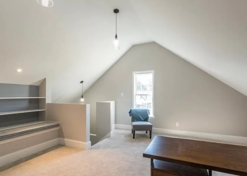Attic room with desk, chair, and built-in shelves. Gray walls, carpet, and two pendant lights.