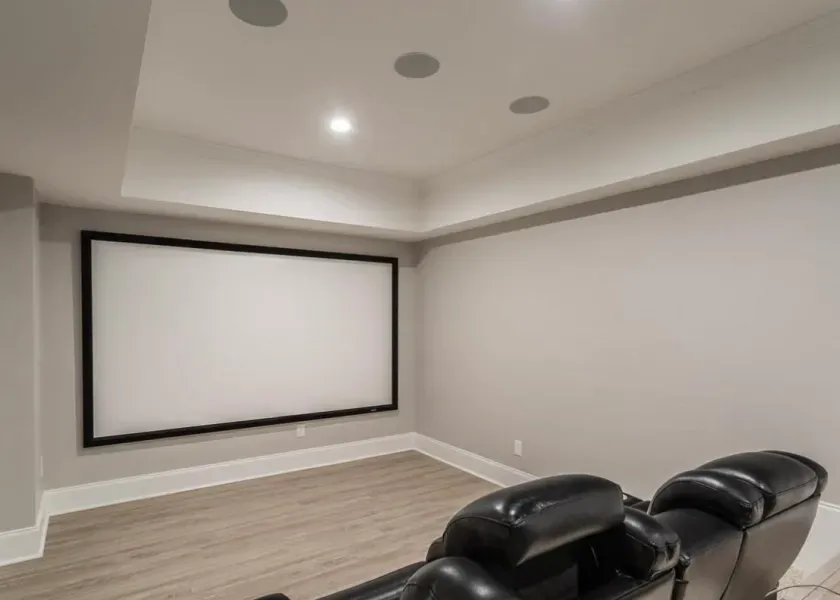 Home theater room with a large screen, black leather recliners, and in-ceiling speakers.