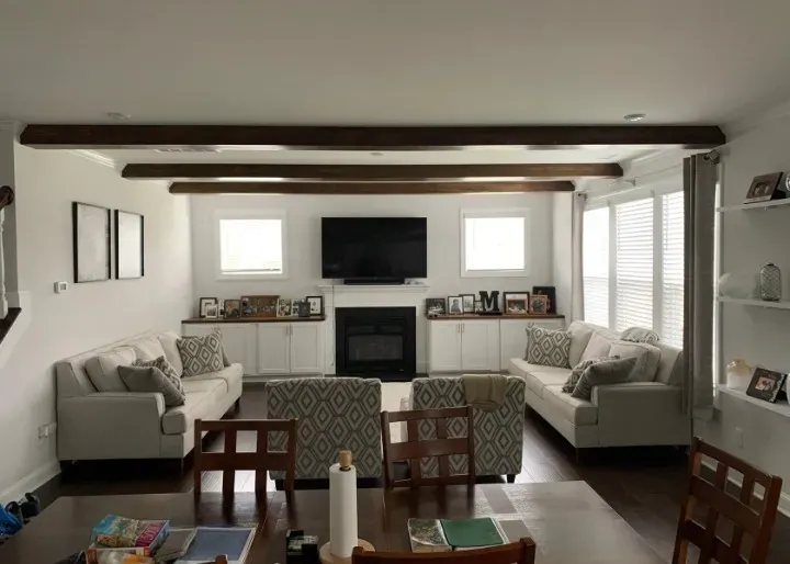 Living room with white walls, dark beams, fireplace, couches, and a dining table.