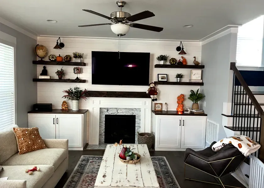 Living room with fireplace, TV, floating shelves, white cabinets, and dark wood floors.