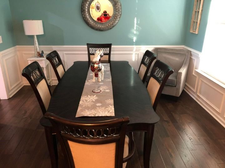 Dining room with a dark table, chairs, and a teal wall. A large mirror hangs above the table.