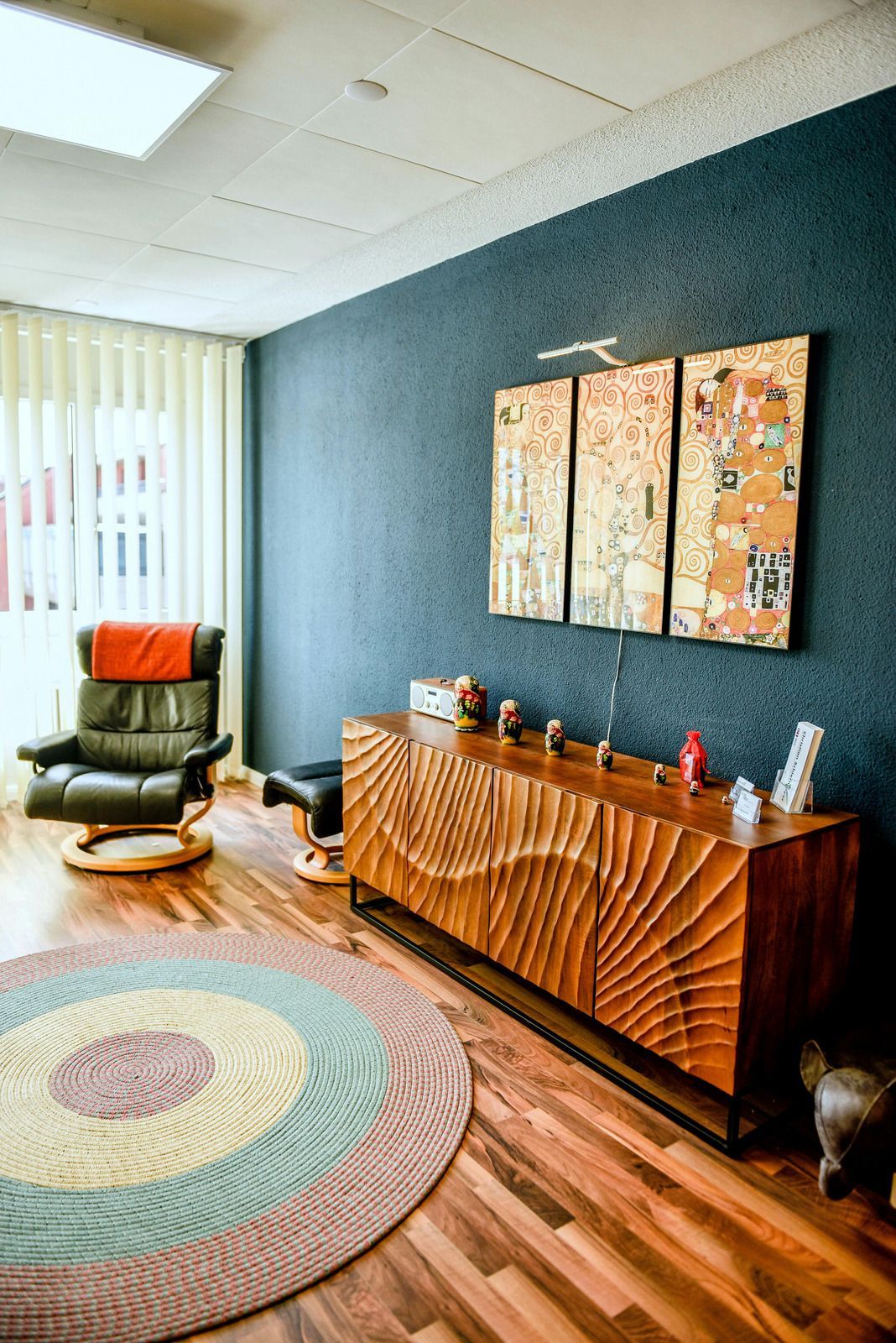 A mid-century modern office space with a wood cabinet, abstract art, chair, and a circular rug.