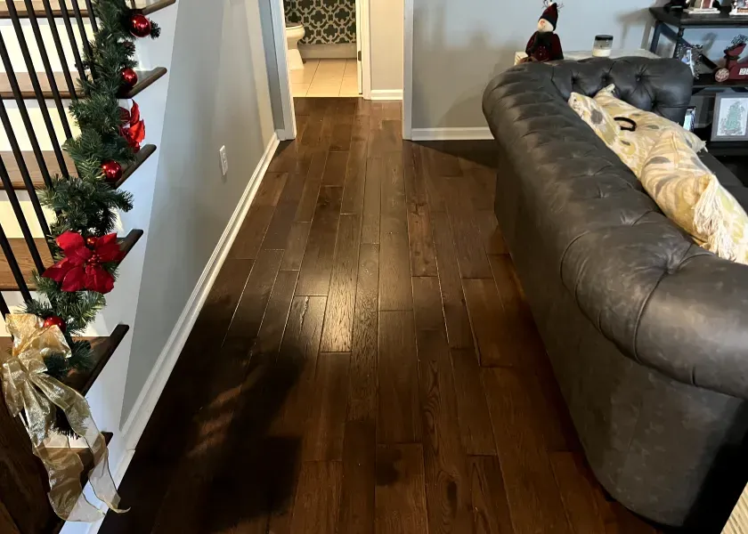 Wooden floor hallway with a staircase on the left decorated for Christmas, and a gray couch on the right.