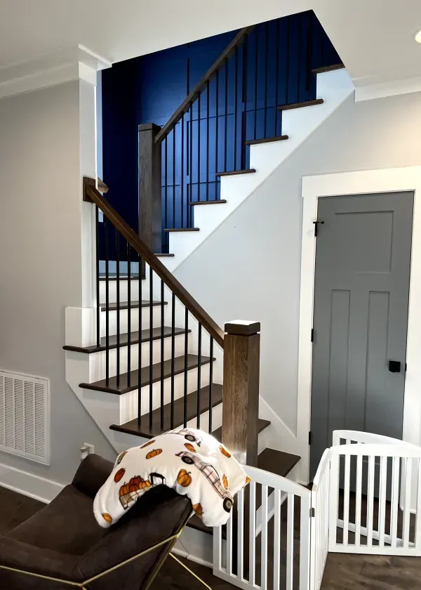 Staircase with brown handrails, black iron balusters, and white risers. Blue accent wall.