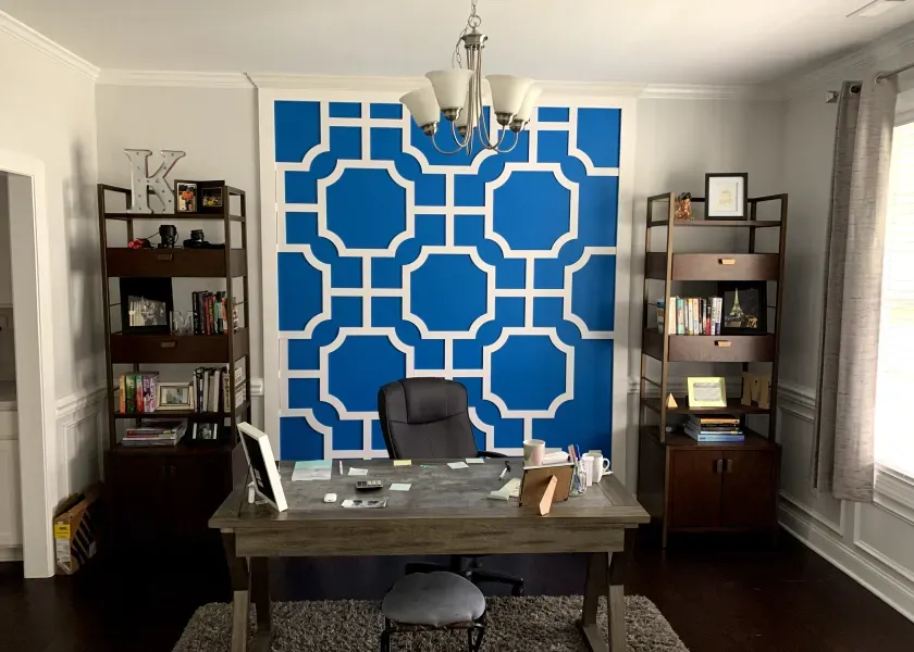 Home office with blue geometric accent wall, desk, shelves, and chair.