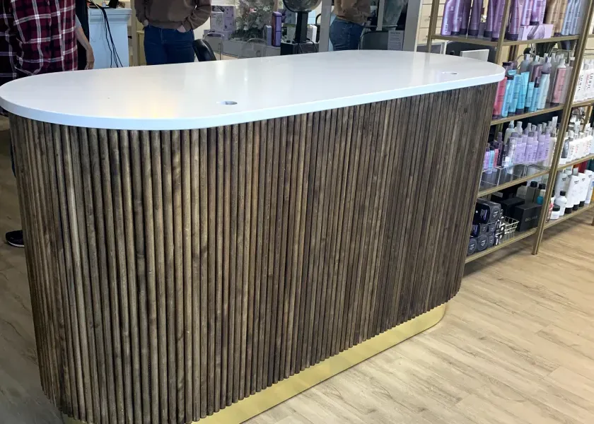 Reception desk with white top, brown wooden vertical slat facade, and gold base.