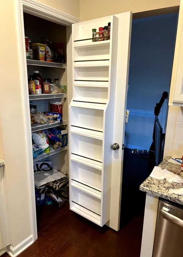 Pantry door with spice rack attached; pantry with wire shelves stocked with food; hardwood floor.
