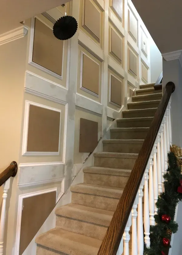 Staircase with beige carpet, paneled wall, and wooden handrails, adorned with Christmas garland.