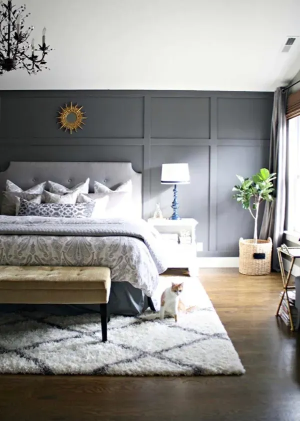 Gray bedroom with tufted headboard, dark paneled wall, a cat, and a bench.