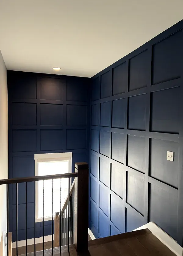 Blue paneled wall in a stairwell with dark wooden steps and railing, white trim, and a window.