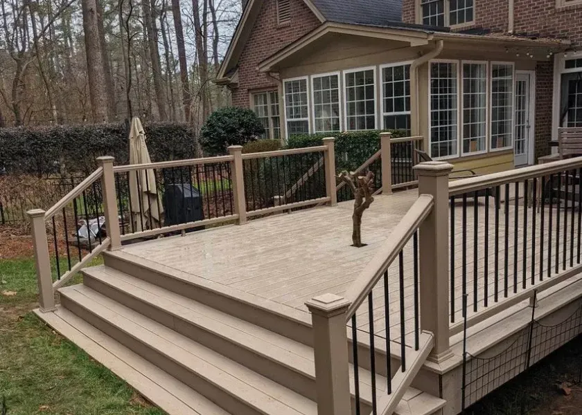Beige deck with steps, black railings, and a house in the background.