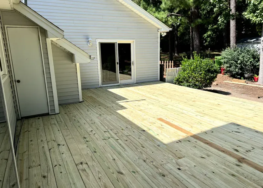 Newly built wooden deck attached to a light gray house with a sliding glass door, outdoors.