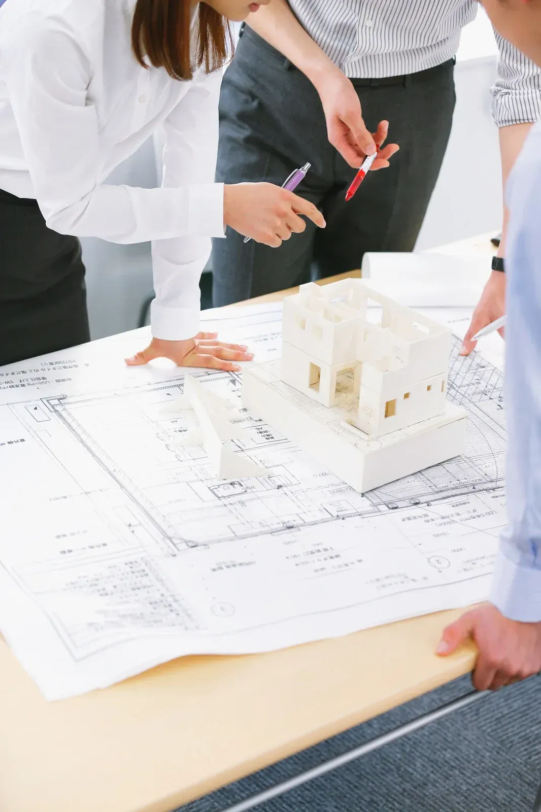 Woman smiling, holding papers, amidst lush indoor plants; wearing a dark green uniform.
