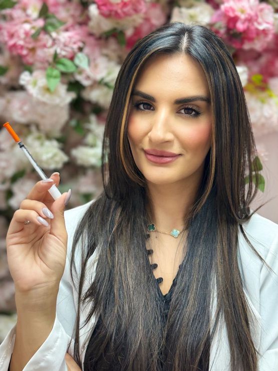 A woman is holding a syringe in her hand in front of flowers.