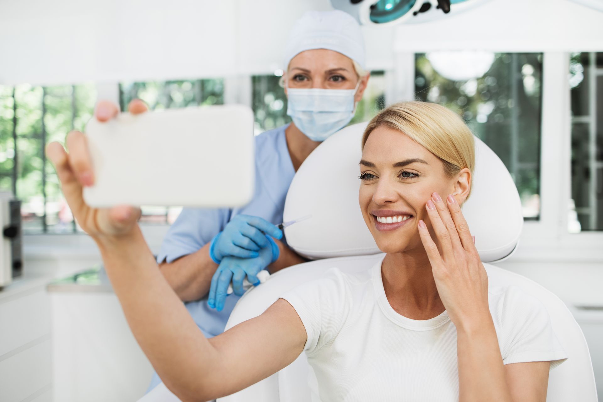 A woman is taking a selfie in a dental chair while a nurse looks on.