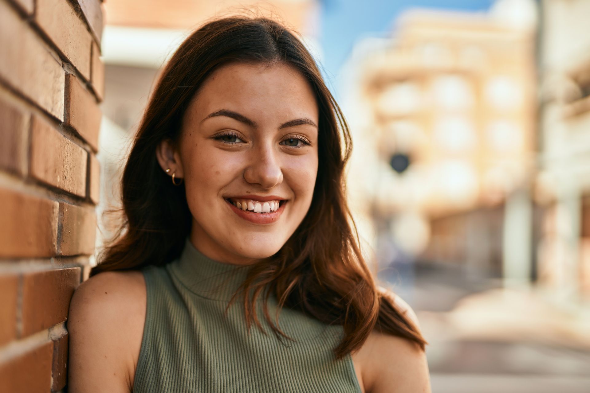 A young woman is leaning against a brick wall and smiling.