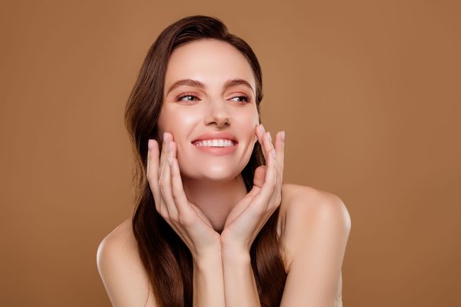 A woman is smiling and touching her face with her hands.