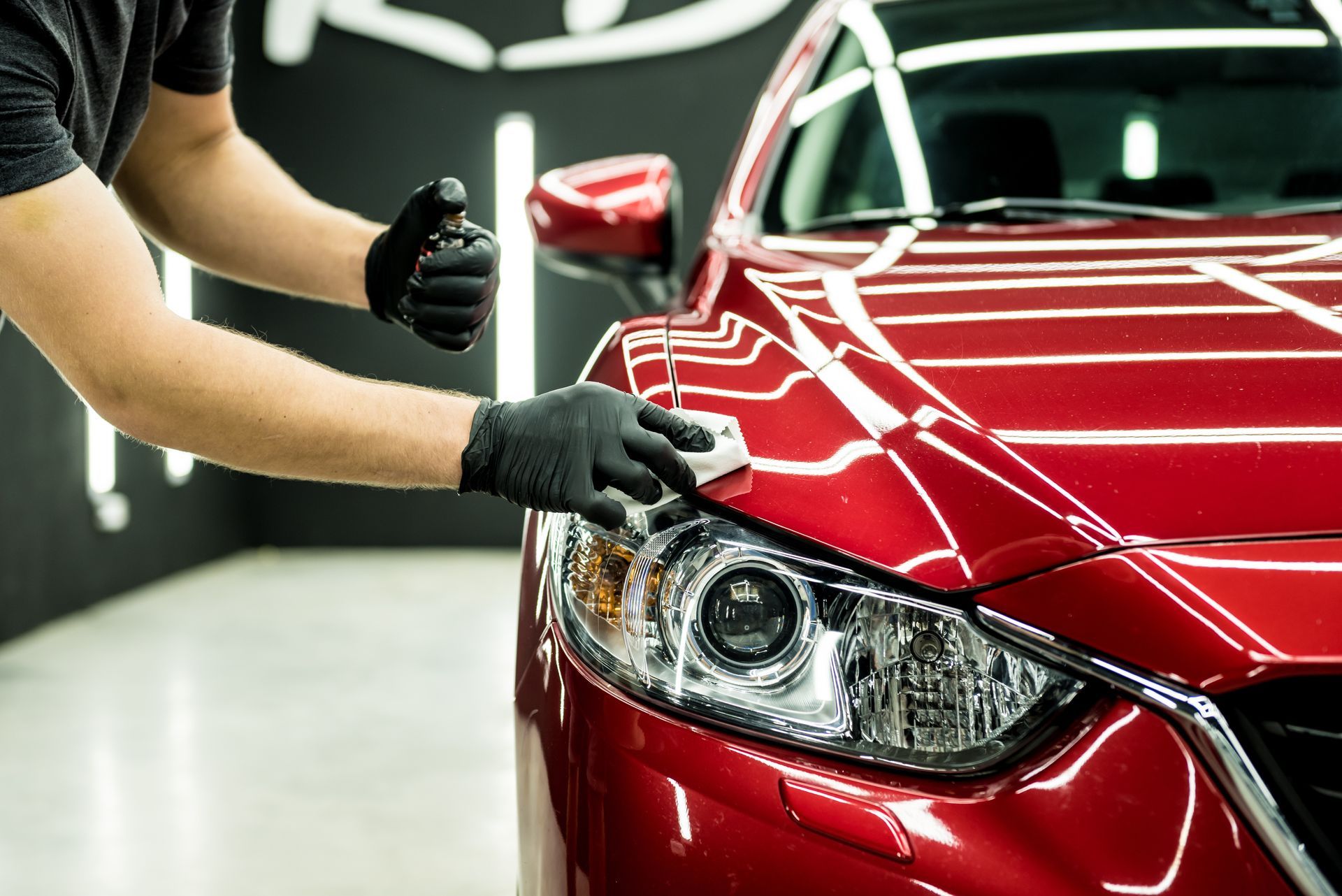 Ceramic coating a red sports car at $99 Tint Club in Yucaipa, CA with a gloved hand polishing the hood