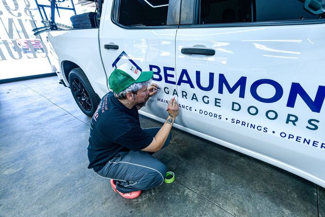 Person adding window tint film to a black car windshield in a bright garage.