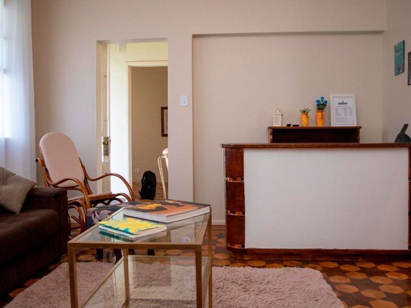 Uma área de recepção com uma mesa de centro, uma cadeira de balanço, um sofá marrom e um balcão branco com objetos decorativos.