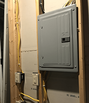 A gray electrical box is hanging on a wooden wall.