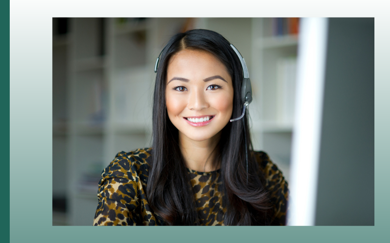 Smiling headset-wearing customer support agent in a patterned top, seated indoors against a blurred office background