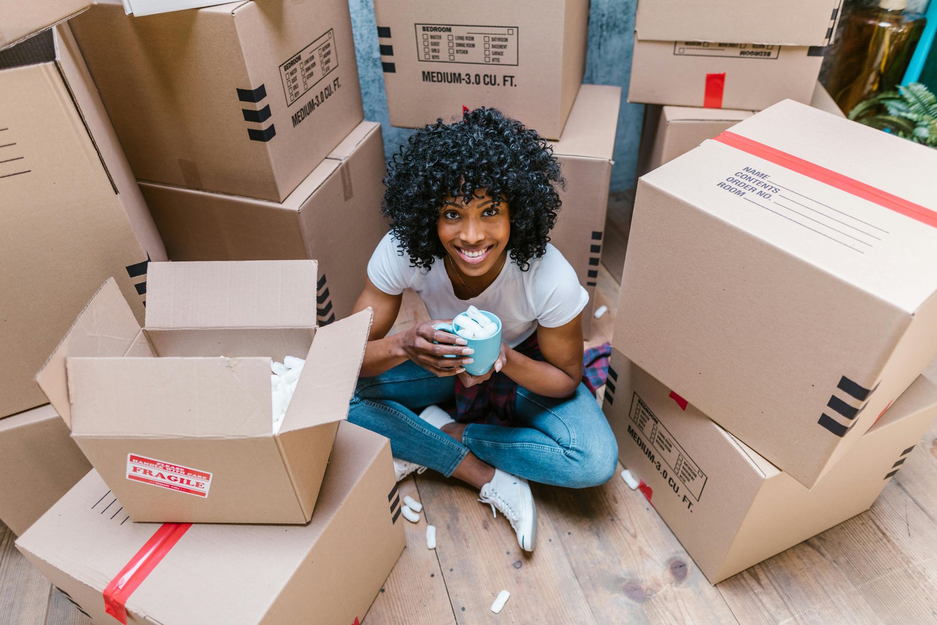 A woman is sitting on the floor surrounded by cardboard boxes.