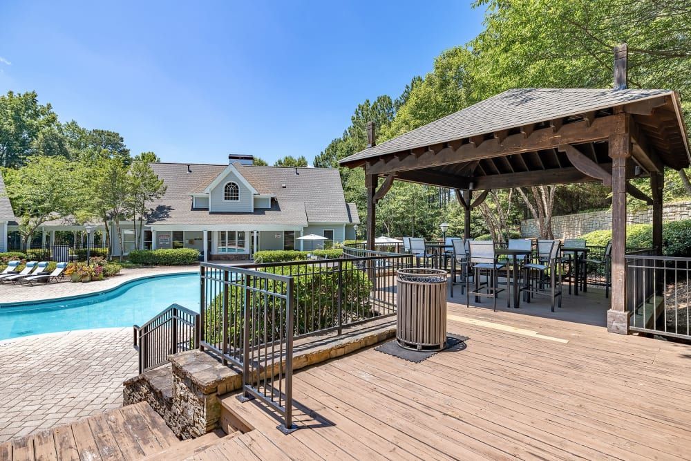 Pool and wooden deck with gazebo for outdoor seating; light blue house in background at Marquis at Sugarloaf, offers apartments for rent in Duluth, GA.