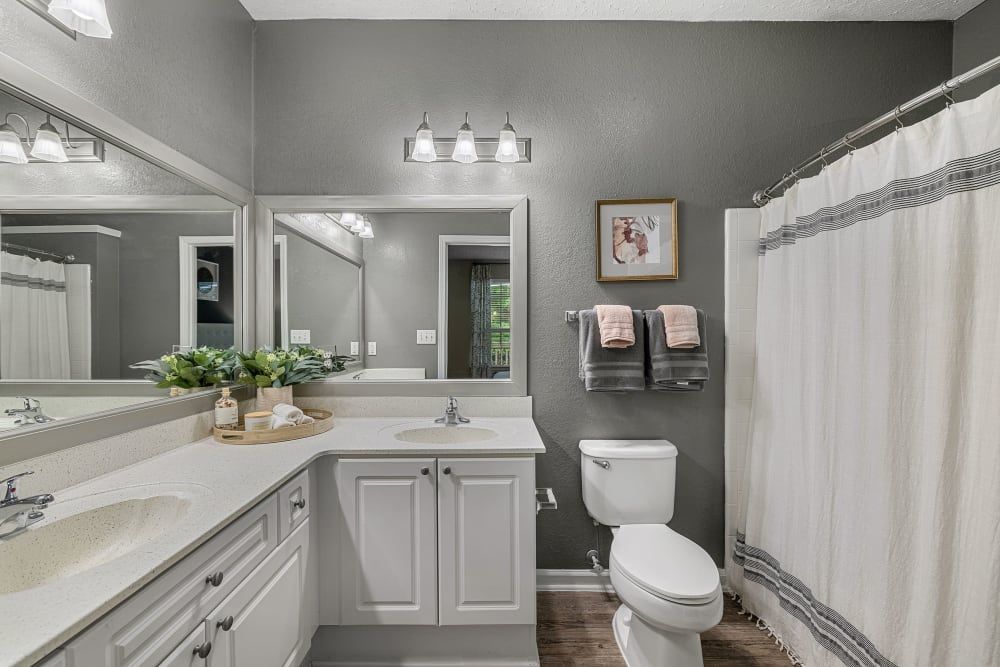 Resort-style bathroom with a toilet, sink, mirror, and shower curtain at Marquis at Sugarloaf, offers apartments for rent near Gwinnett Medical Center.