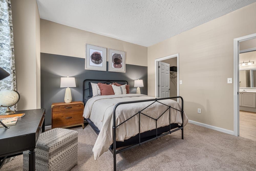 Modern bedroom with a bed, nightstand, desk, and lamps at Marquis at Sugarloaf in Duluth, GA.
