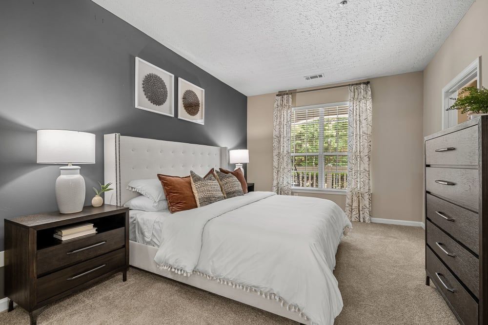 Spacious bedroom with a bed, dresser, nightstand and window at Marquis at Sugarloaf, offers apartments in Gwinnett County,