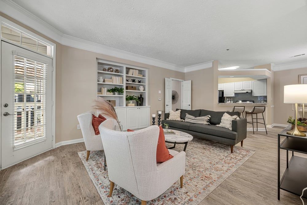 Cozy living room with white chairs, a gray sofa, and an open kitchen at Marquis at Sugarloaf, offers apartments in Gwinnett County,