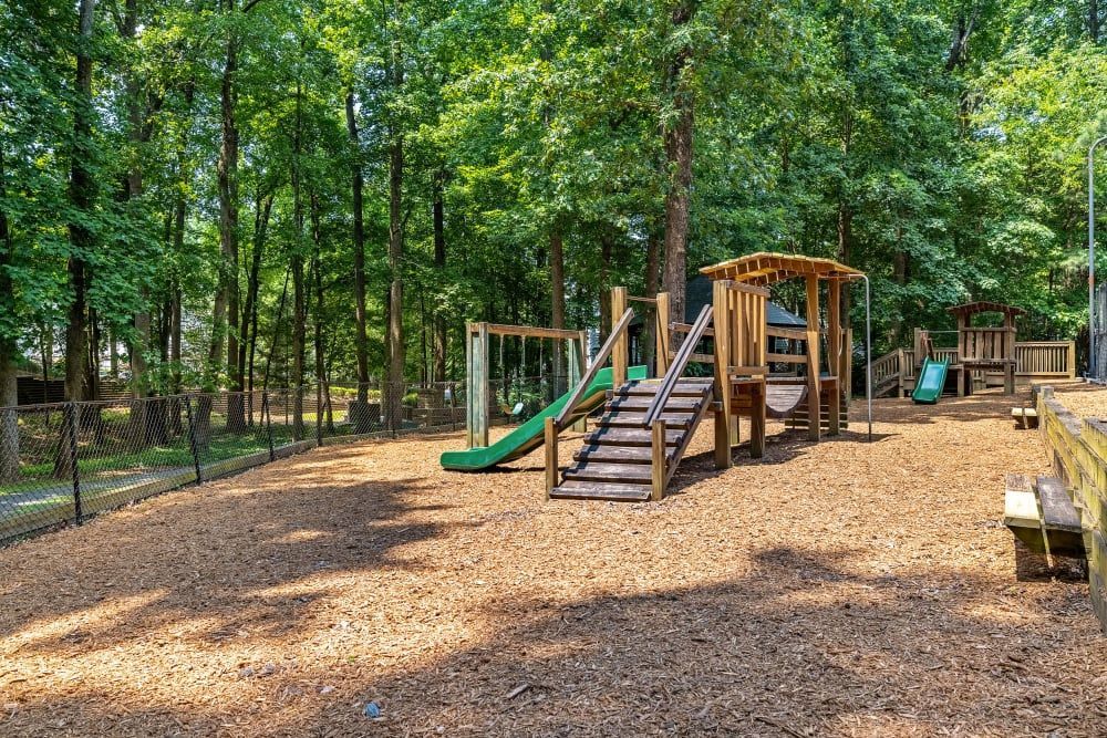 Playground with wooden structures, swings, and a slide on a wood chip surface, surrounded by trees at Marquis at Sugarloaf, offers apartments for rent in Duluth, GA.