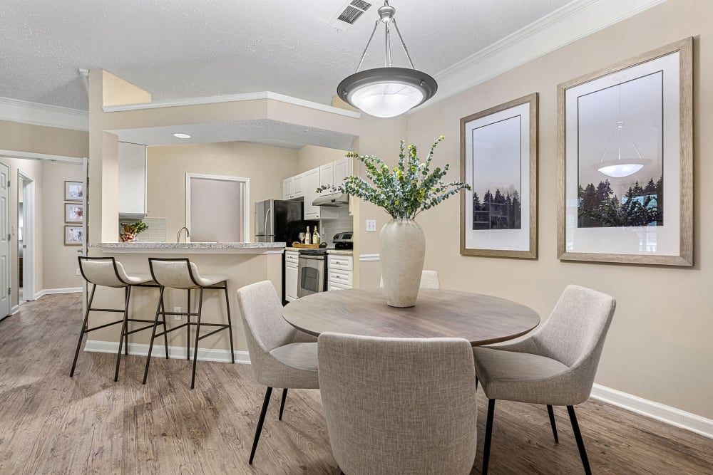 Dining area with wooden table, gray chairs, and open kitchen with bar stools at Marquis at Sugarloaf, offers apartments near Sugarloaf Mills.