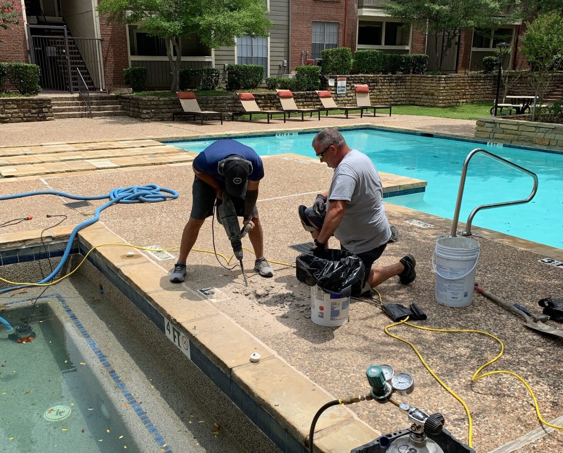Two men are working on the side of a swimming pool.
