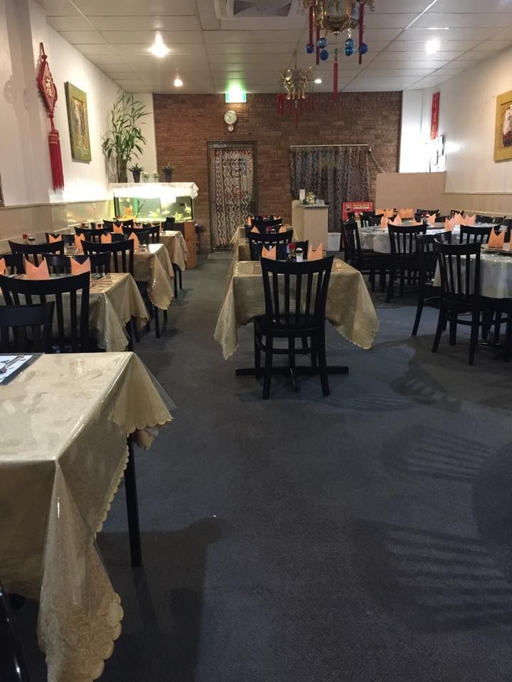 A restaurant interior with several tables covered in tan tablecloths and black chairs, set against a brick back wall.