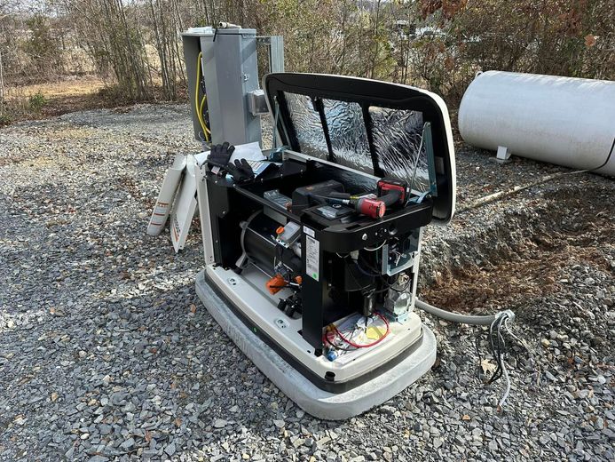 Generator with open cover, in a gravel area with large white tanks in the background.