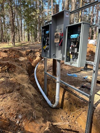 Electrical boxes mounted on a post, with conduit running through a trench in a wooded area.