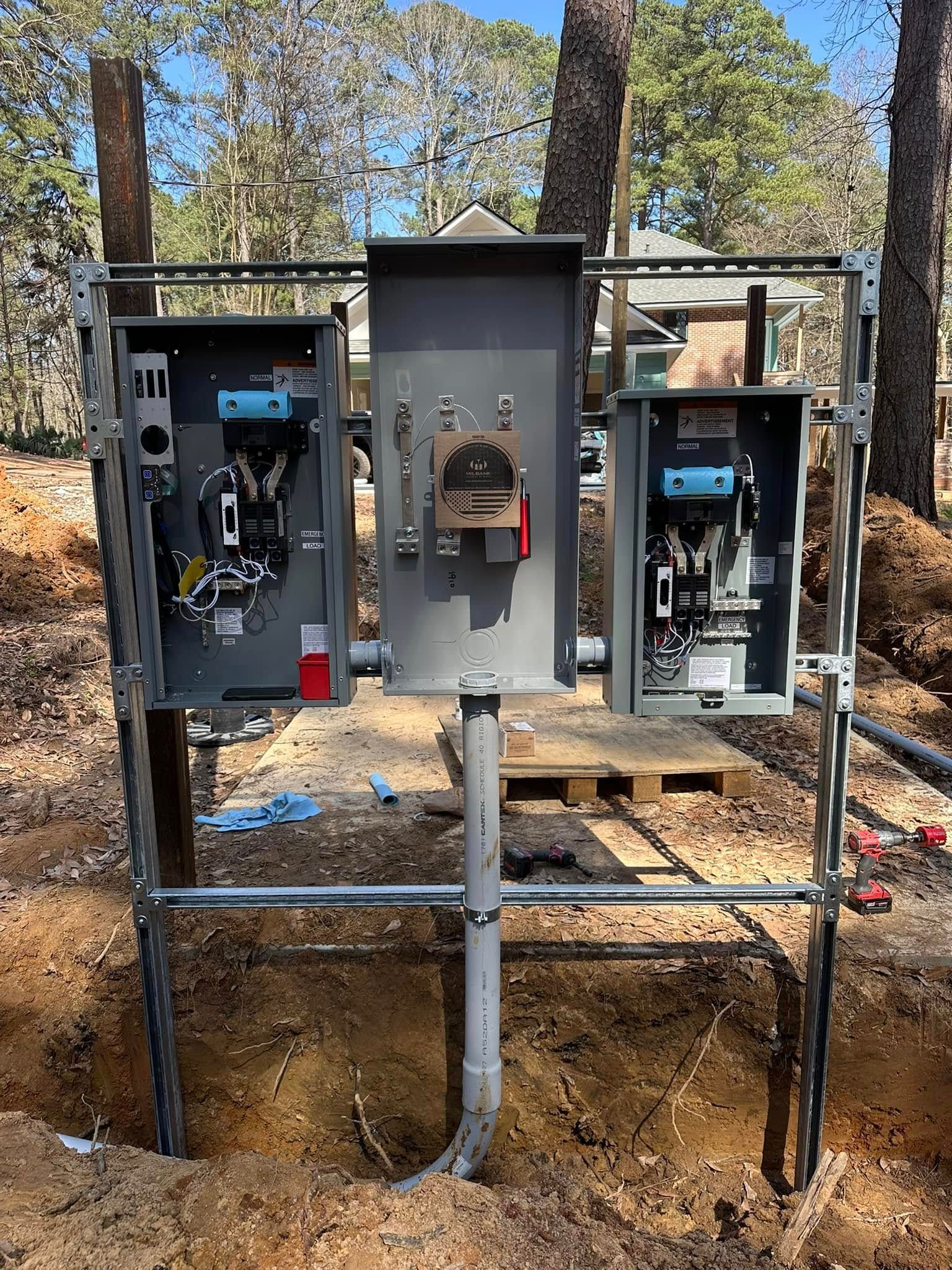 Electrical panel setup outdoors, grey metal boxes, conduit, and scaffolding in a dirt excavation.
