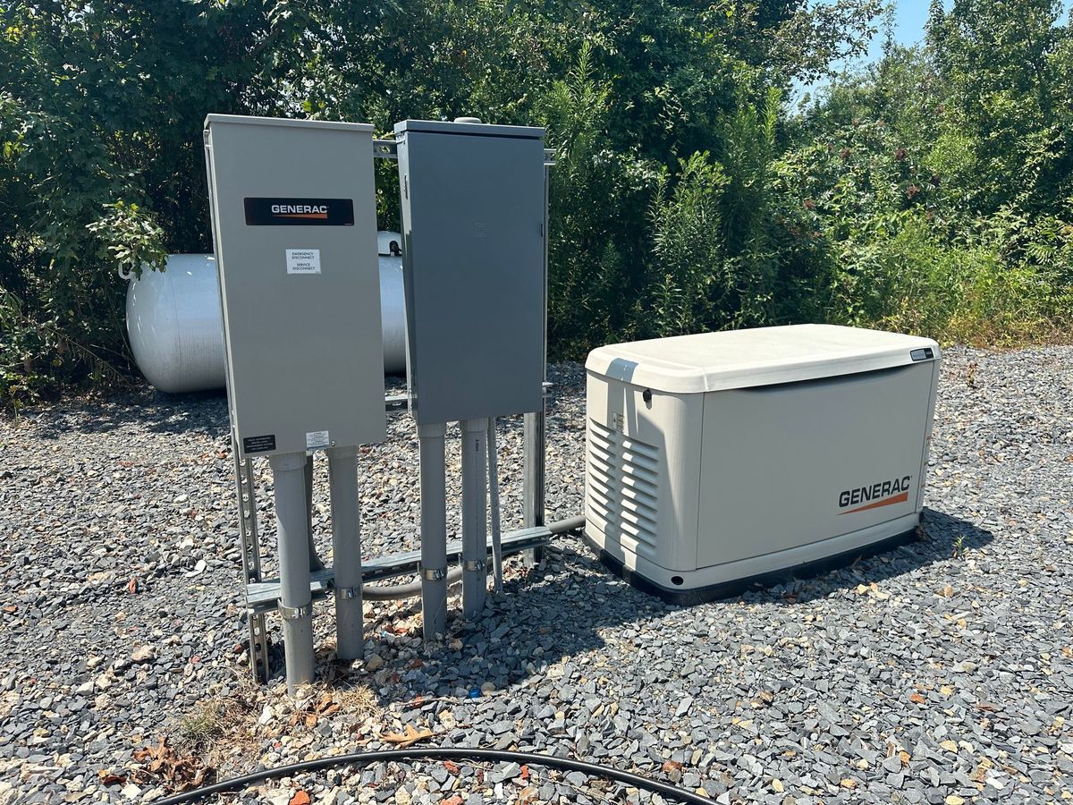 Backup generator system with two gray electrical boxes and a beige generator on a gravel surface.