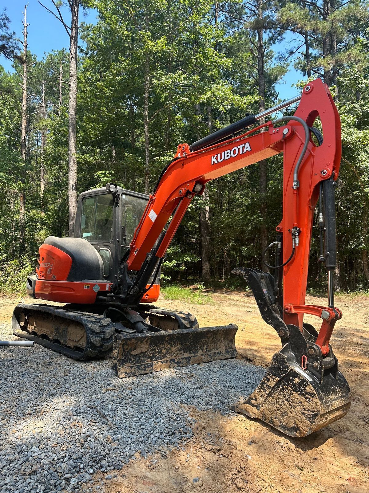 Orange Kubota excavator on a gravel surface near trees.