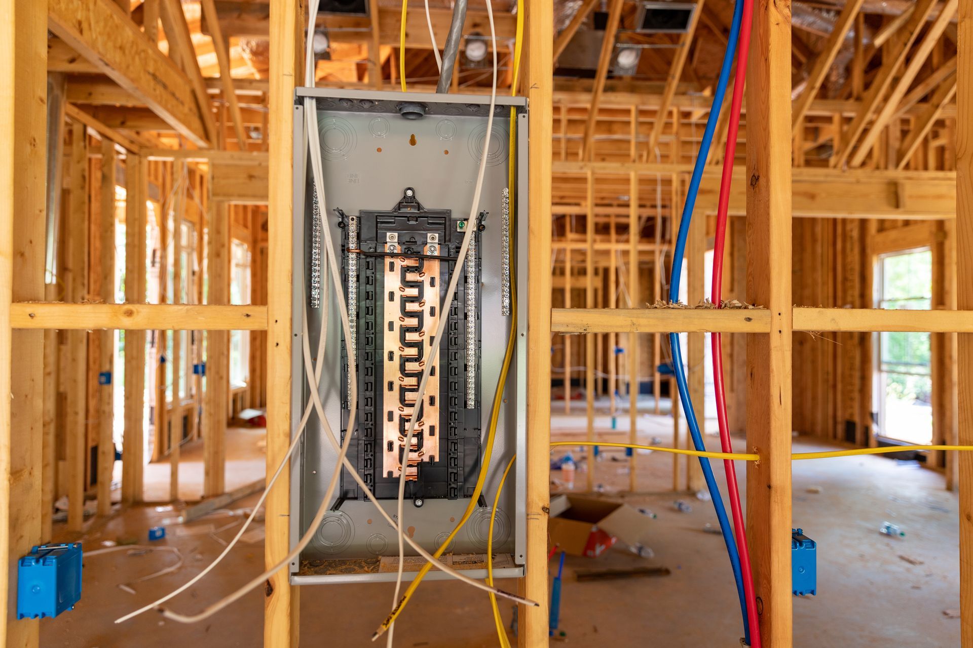 Construction framing with electrical panel and wiring visible. Interior view, wooden studs, wires of multiple colors.