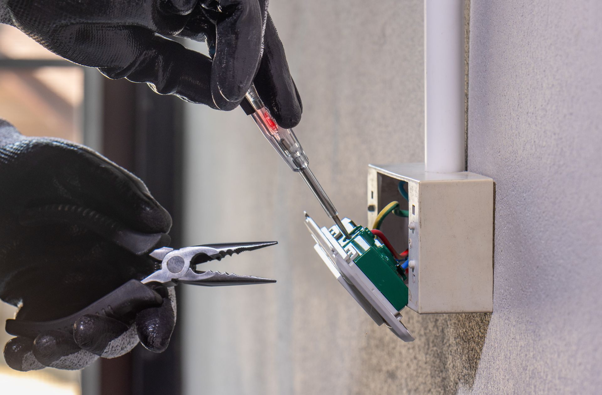 Electrician installing an outlet, using tools and wearing black gloves.